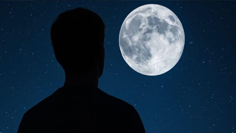 Silhouette d’une personne observant la Lune dans un ciel étoilé.