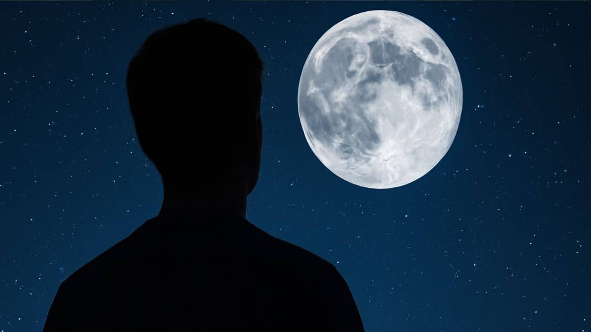 Silhouette d’une personne observant la Lune dans un ciel étoilé.
